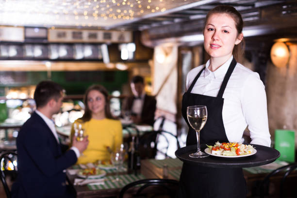 Portrait of smiling female waiter who is standing with tray in restaurant